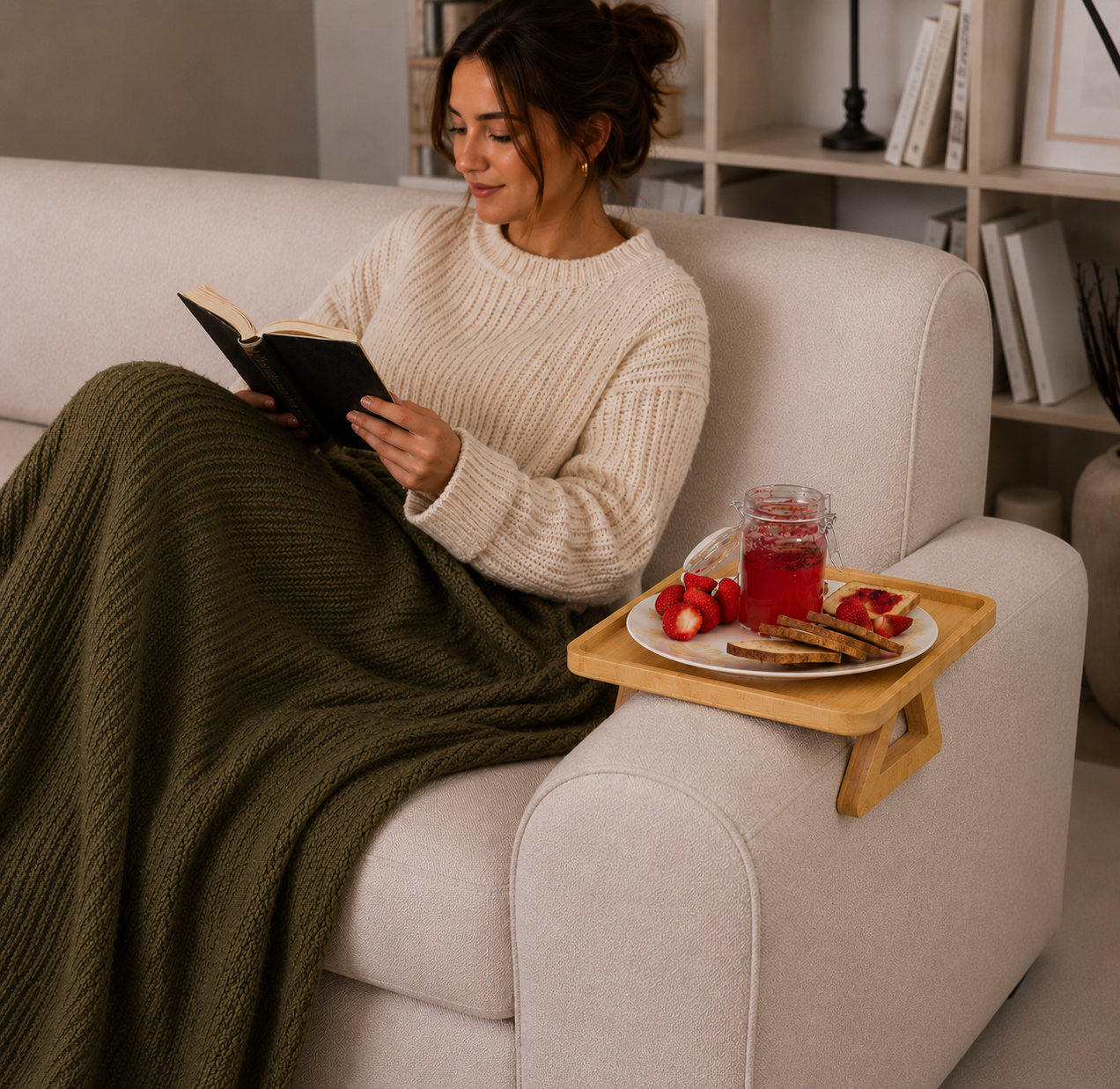 Woman reading a book on a couch with a tray of food and drink beside her